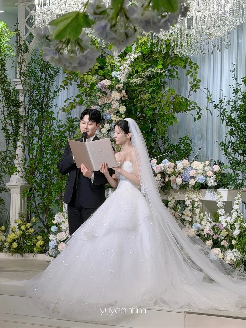초록빛 꽃 장식 앞에서 서약하는 두 사람